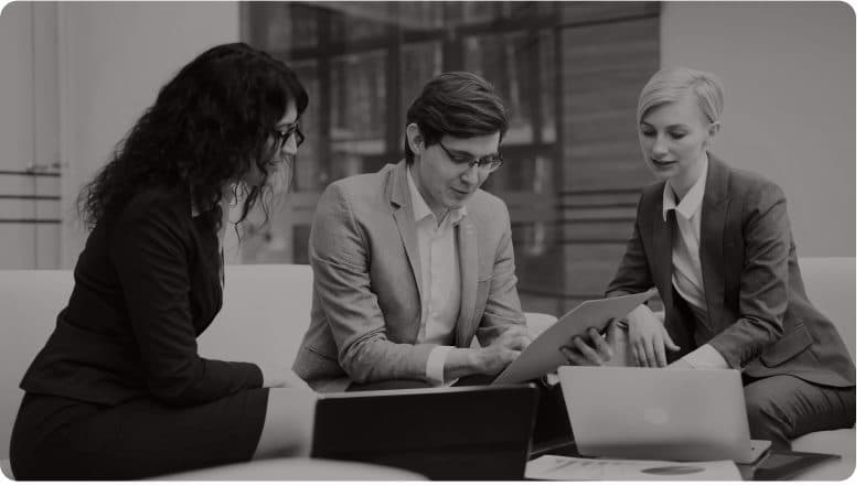 Three colleagues working through paperwork around a laptop