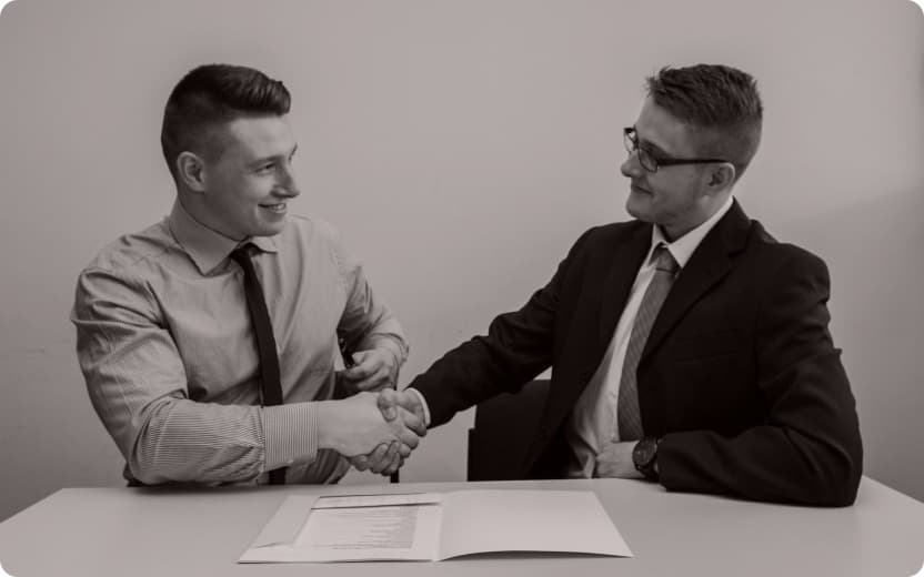 Two people shaking hands over a signed contract